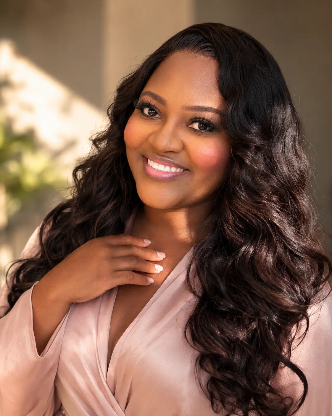 Portrait of Fabiola Robert smiling warmly in a soft blush satin robe, her hair in loose waves